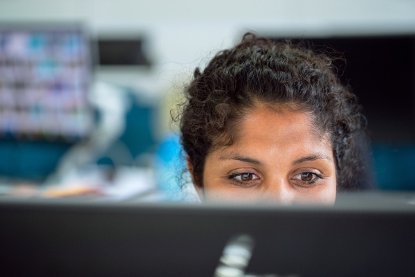 Young woman with dark curly hair working in front of a screen which is obscuring the lower part of her face